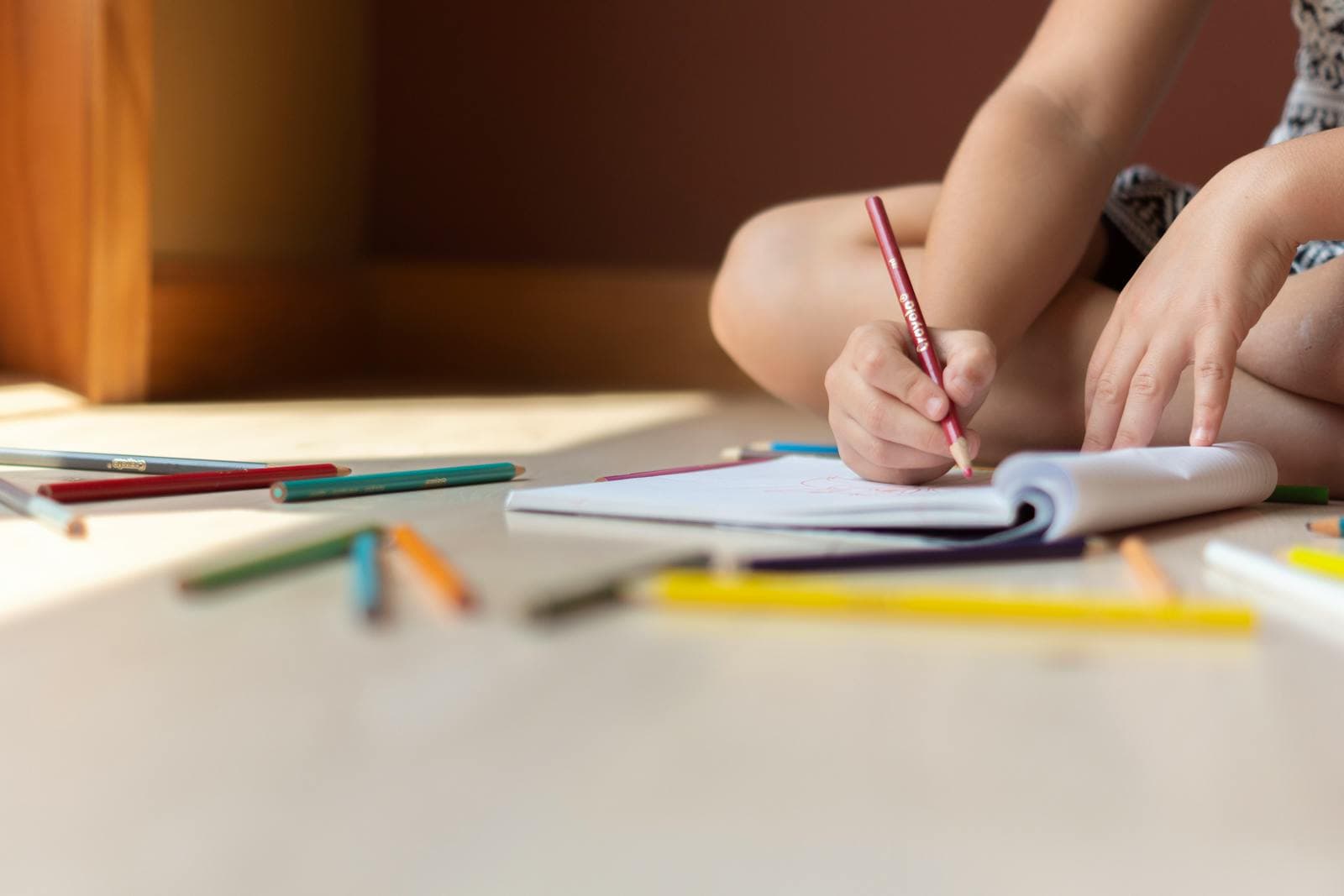 Child coloring in a notebook with pencils scattered around