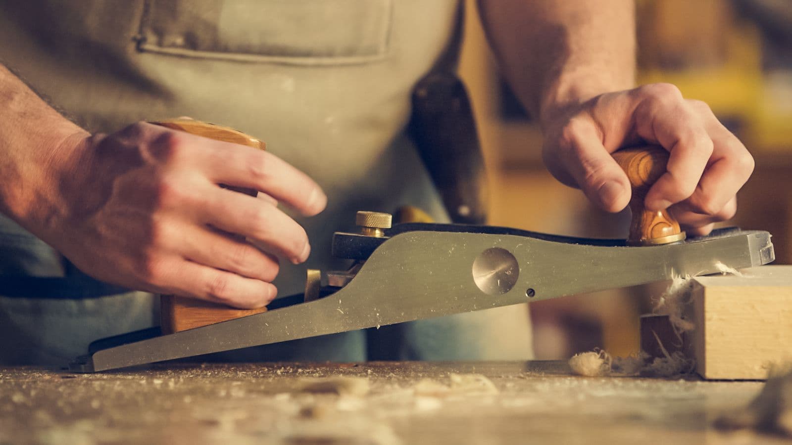 Hands guiding a wood planer across lumber