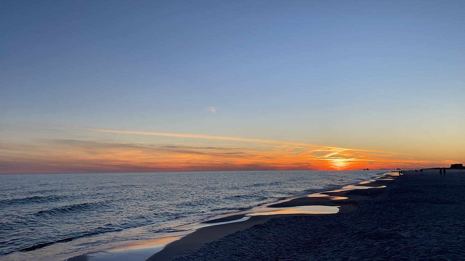 Sunset over the Gulf of Mexico at Gulf Shores, with orange light reflecting off gentle waves along the white-sand shoreline.