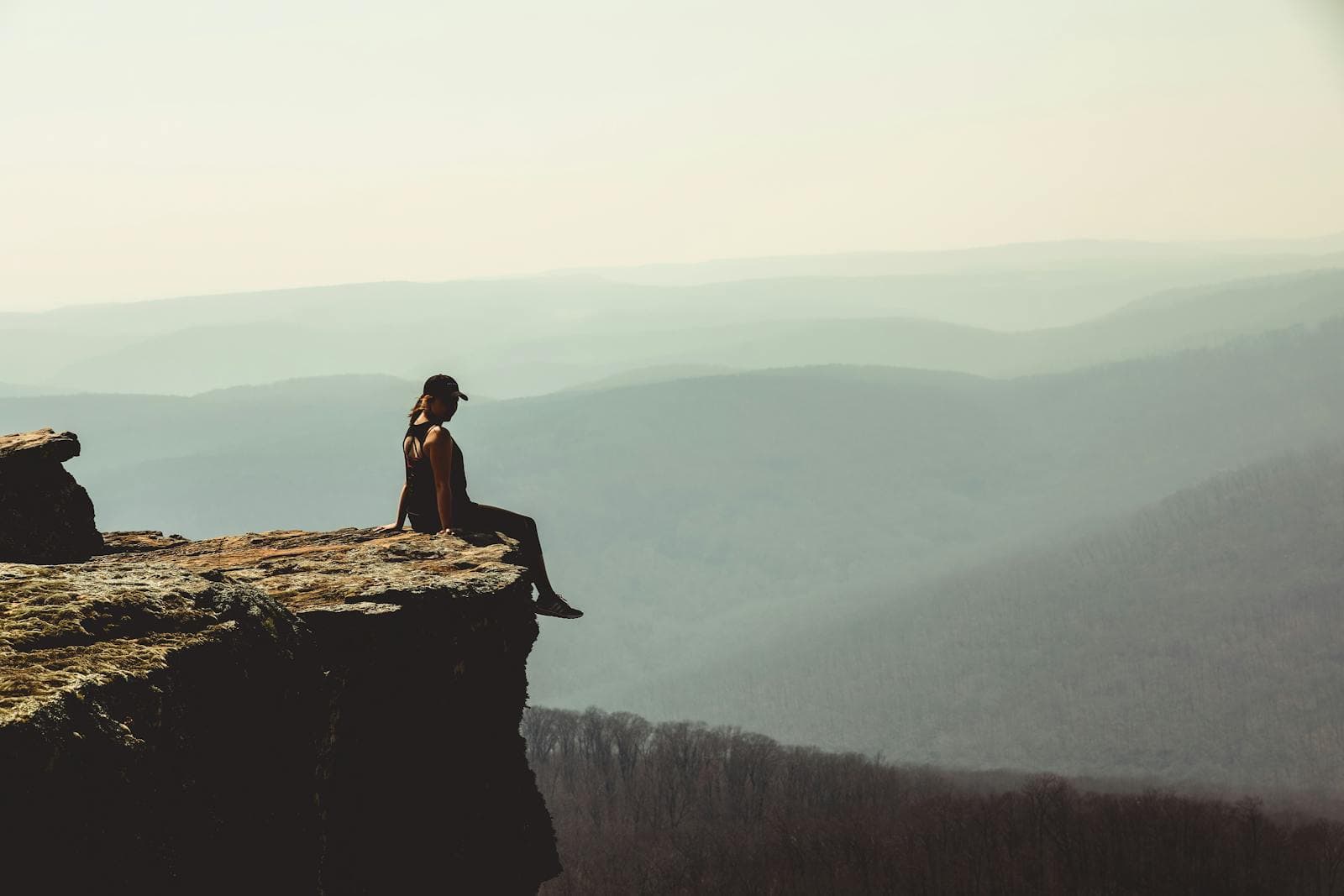 A hiker sits on a rocky bluff overlooking layered, hazy ridgelines of the Ozark Mountains near Winslow, Arkansas.
