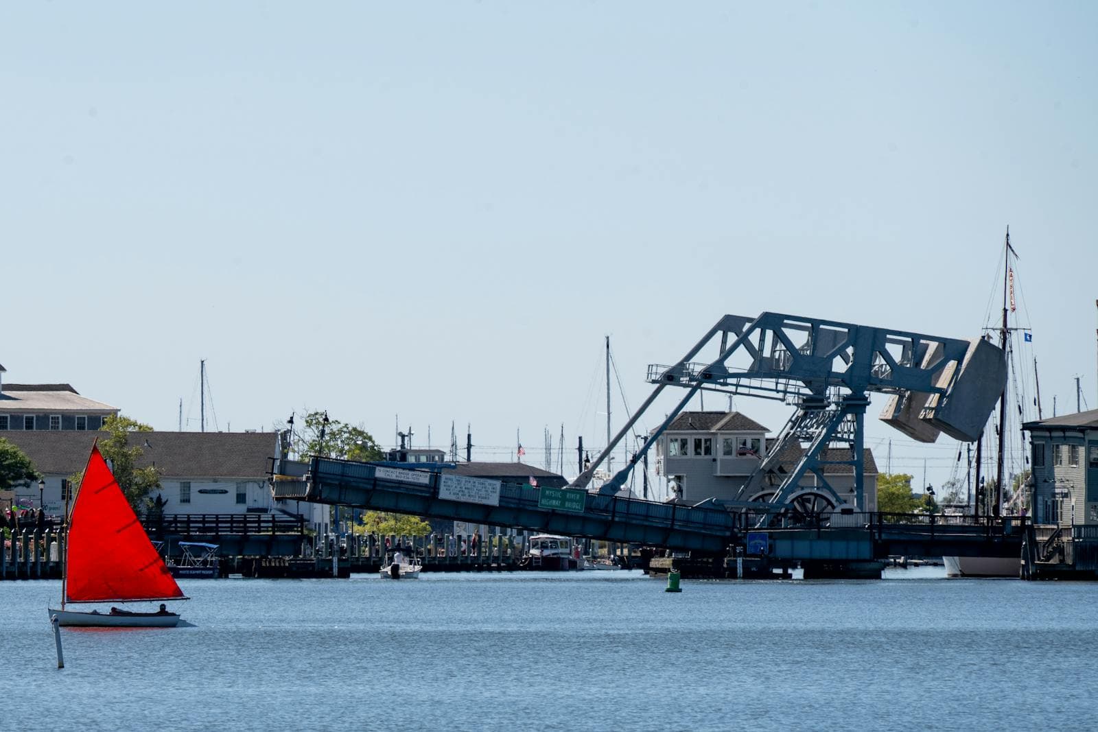 A red sailboat passes the historic Mystic River drawbridge on a calm day in Mystic, Connecticut.