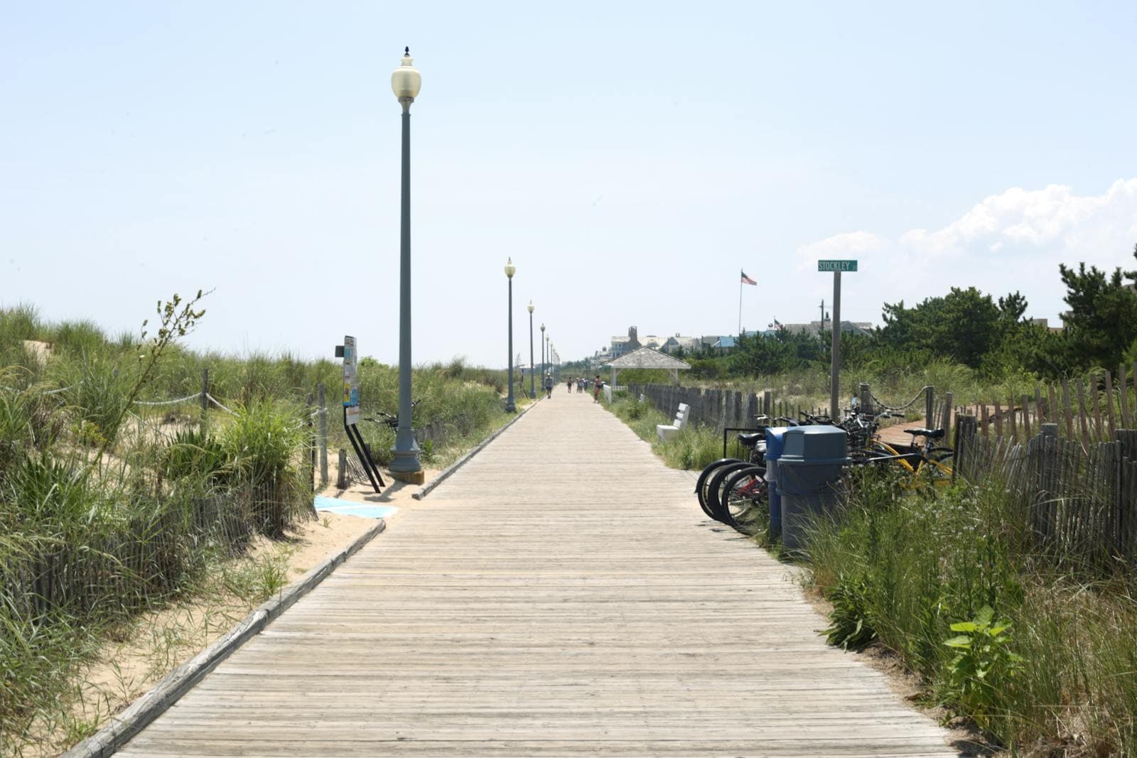 Sun-washed wooden boardwalk lined with dune grass, lampposts and parked bicycles at Rehoboth Beach.