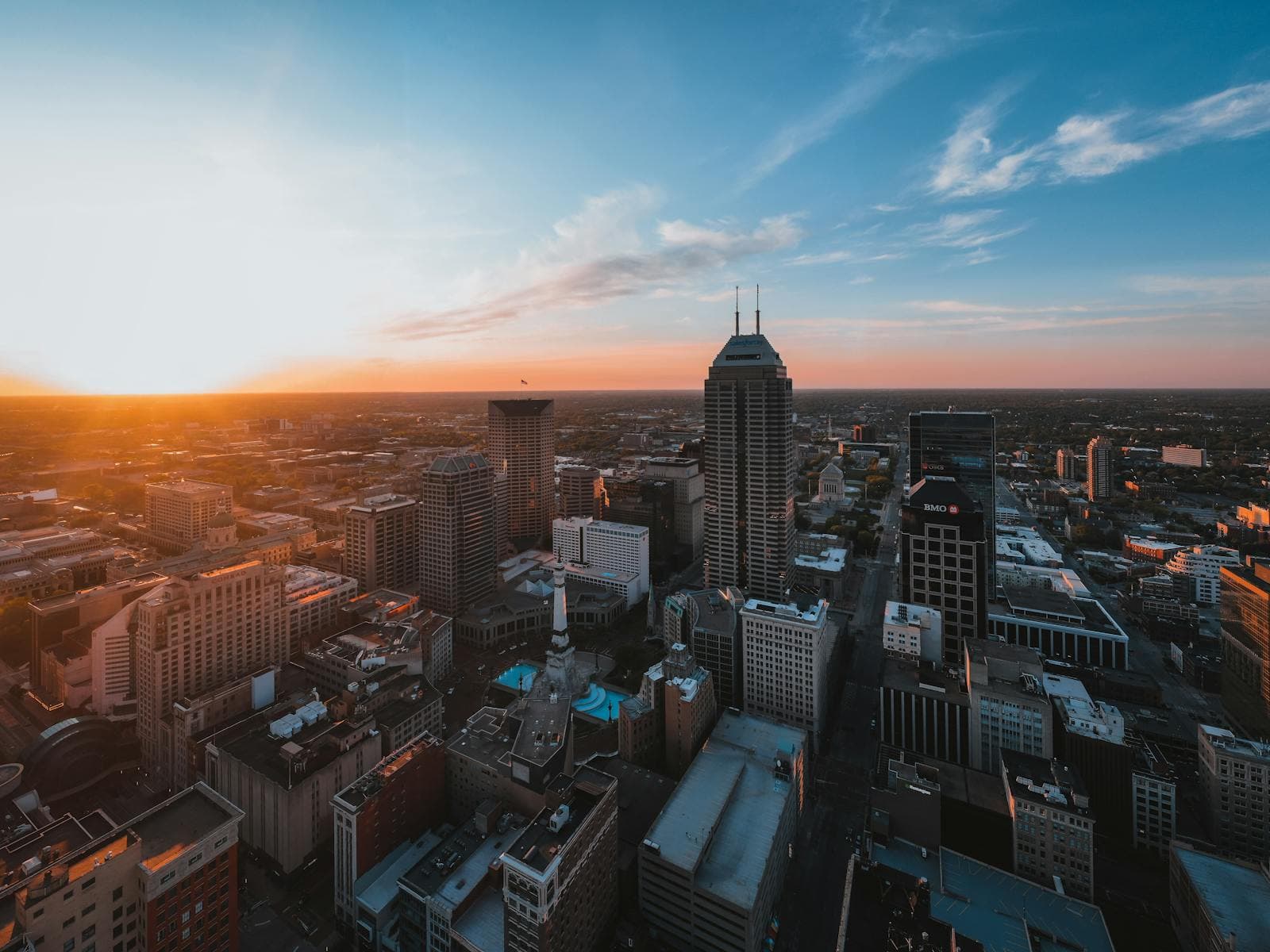 Aerial view of downtown Indianapolis and Monument Circle glowing under a golden sunset.