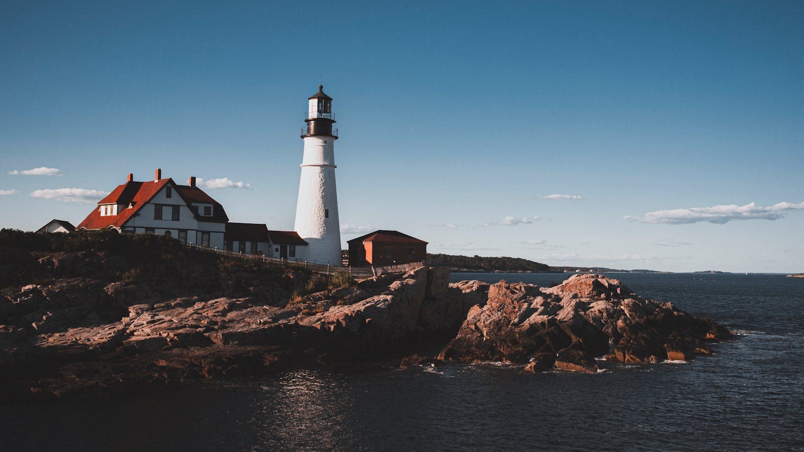 Portland Head Light lighthouse stands on the rocky Maine coastline beside the keeper's house overlooking the Atlantic Ocean.