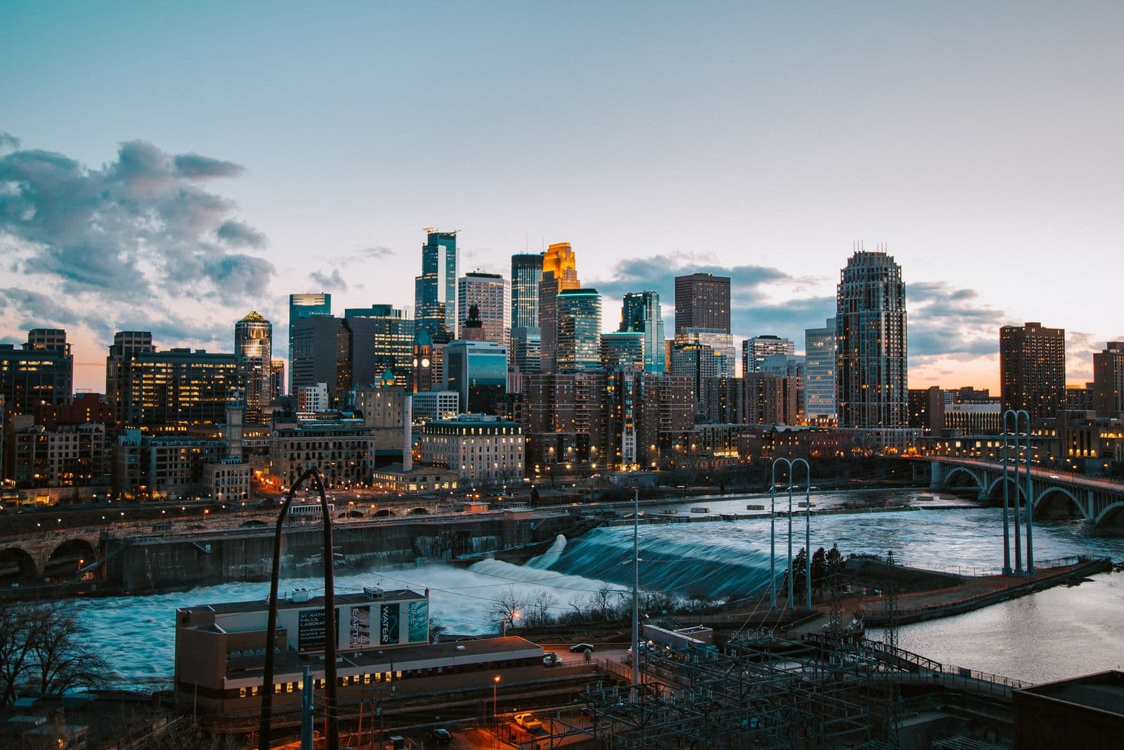 The Minneapolis skyline above St. Anthony Falls and the Mississippi River bridges at dusk.