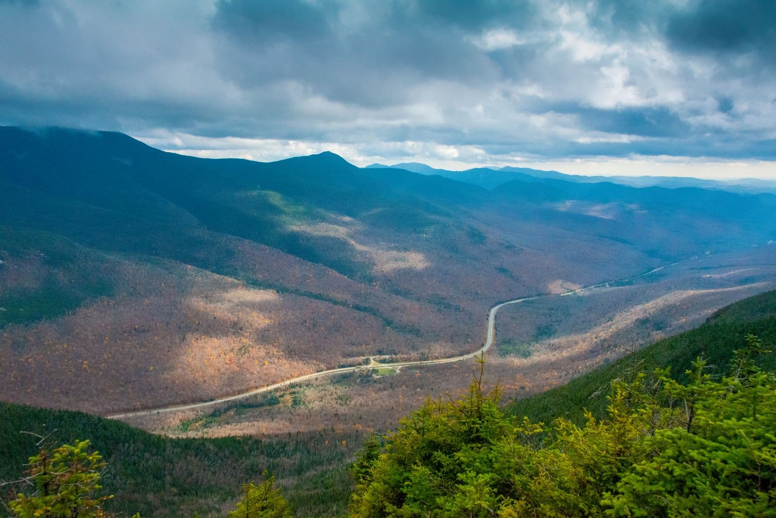 A panoramic overlook of a White Mountains valley road winding through vibrant fall foliage in New Hampshire.