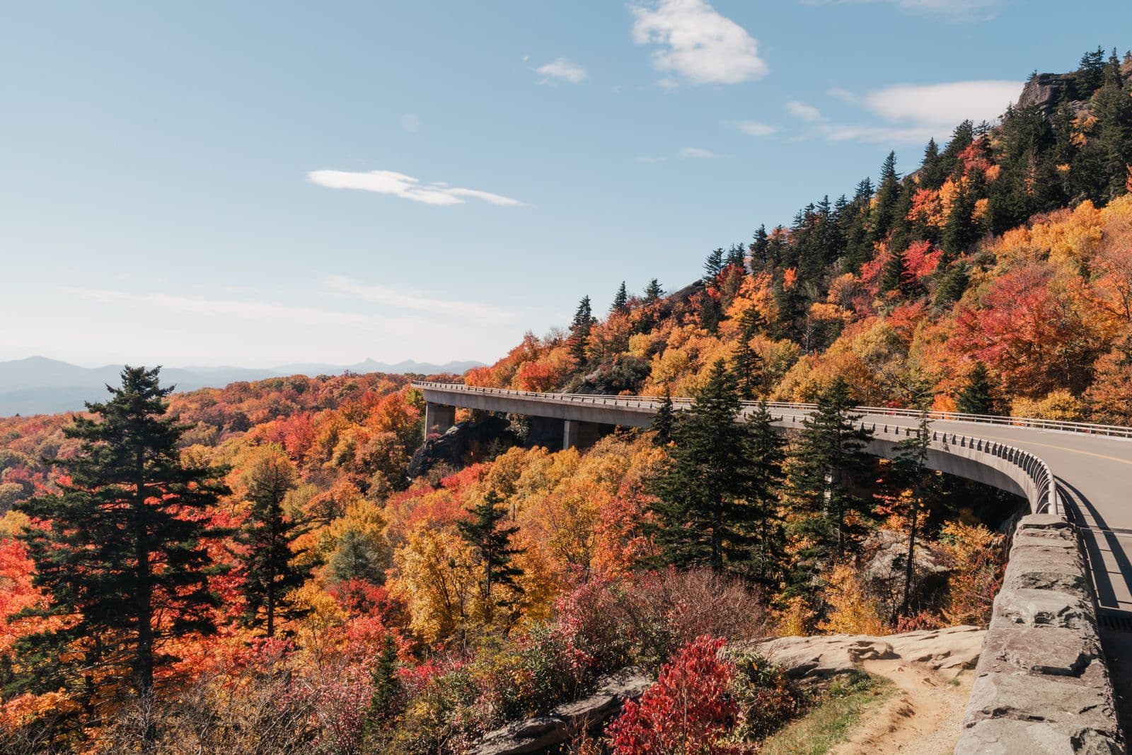 The Linn Cove Viaduct curves along a mountainside ablaze with red and orange autumn foliage on the Blue Ridge Parkway.