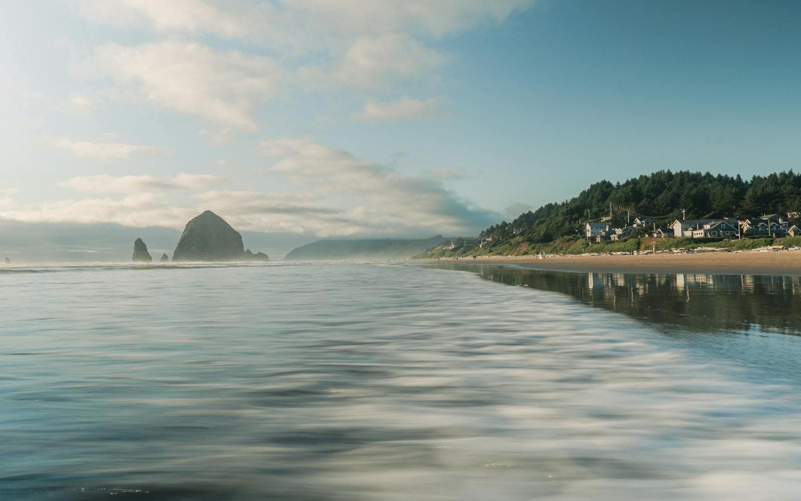 Haystack Rock stands offshore at Cannon Beach, Oregon, mirrored in wet sand on a soft morning.