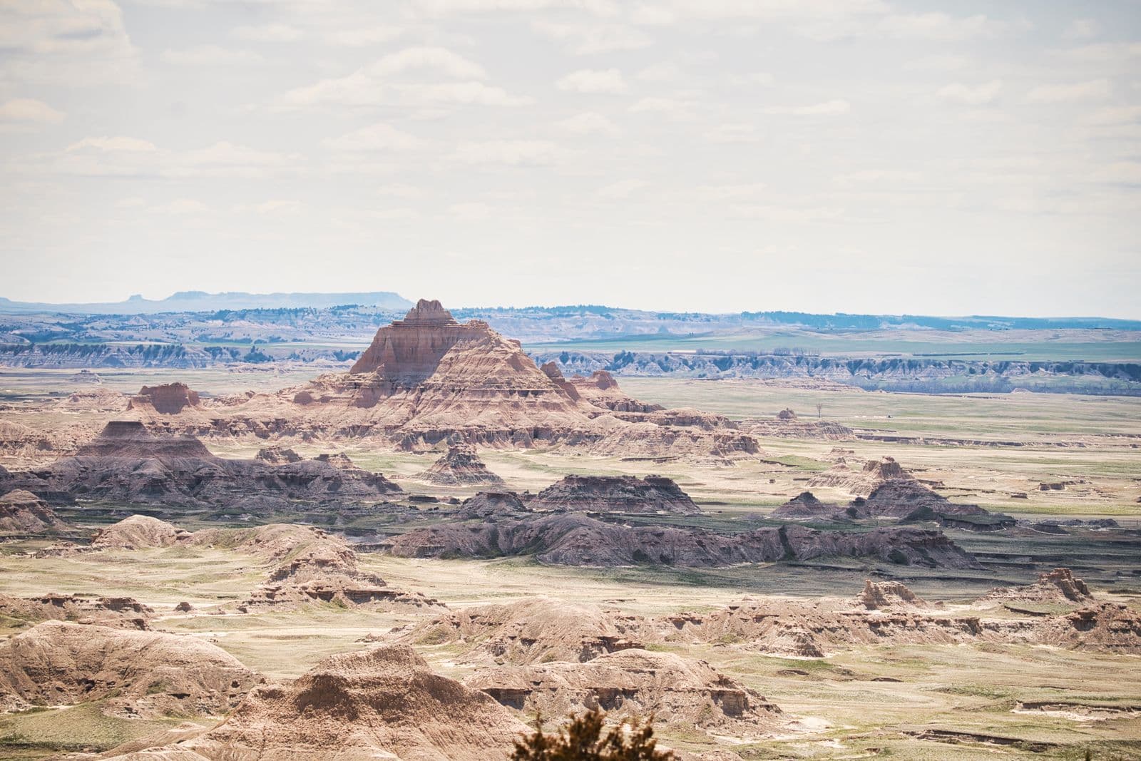Jagged striped rock formations of Badlands National Park spreading across a vast prairie under a hazy sky.