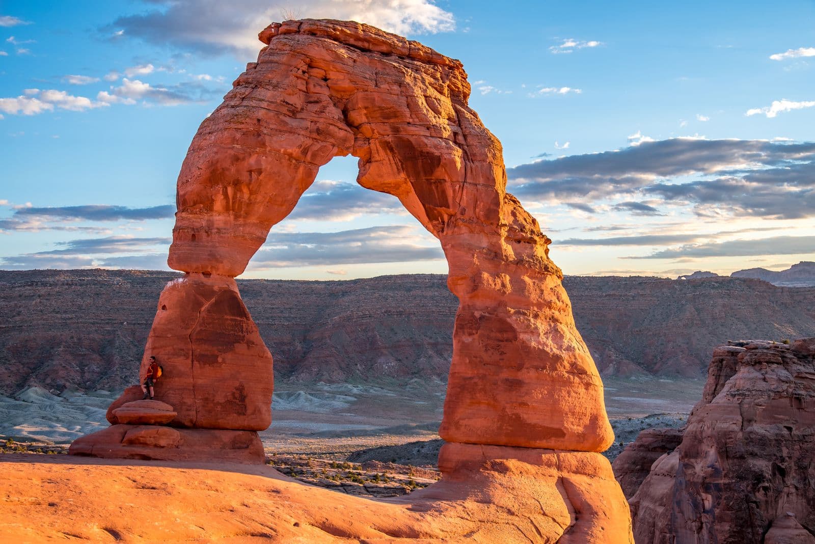 Delicate Arch glows orange in golden-hour light above the slickrock bowl of Arches National Park.