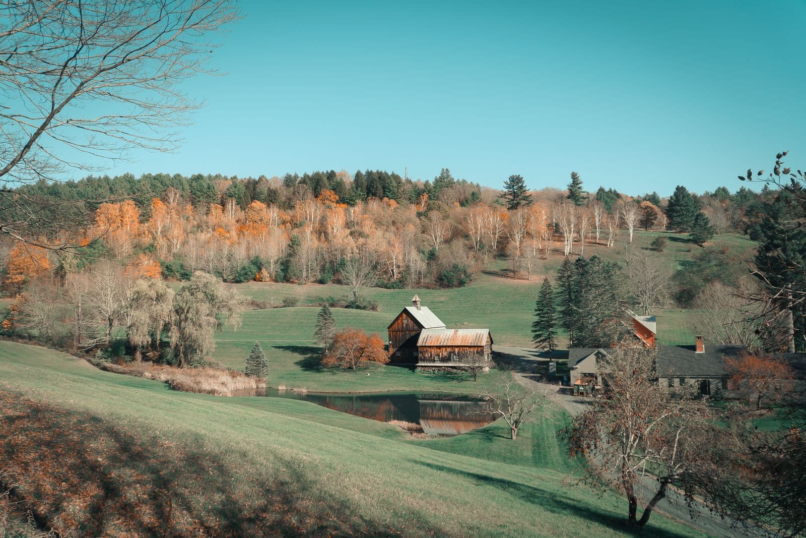 A classic farmhouse and red barn sit among rolling hills of brilliant autumn foliage in Woodstock, Vermont.