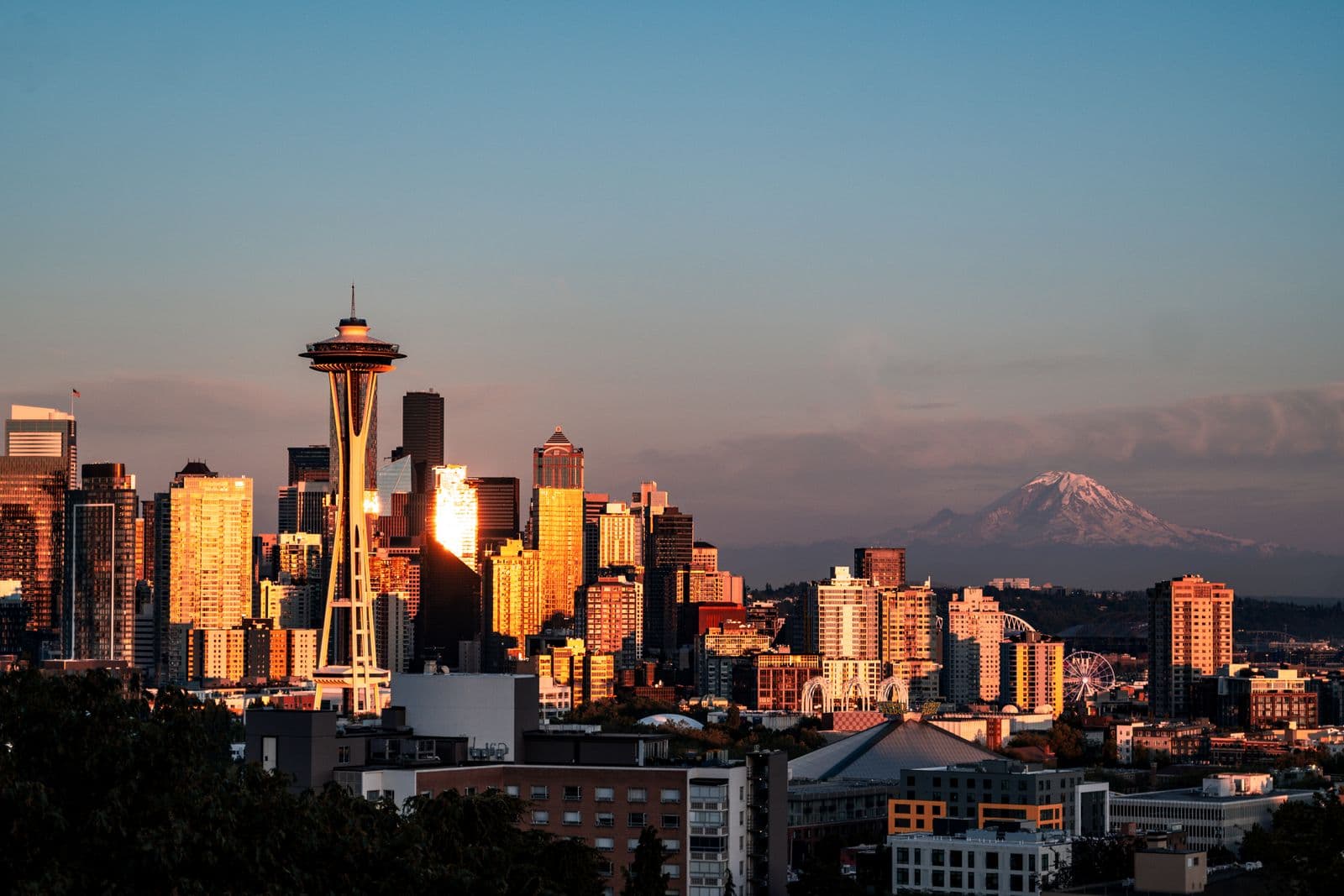 The Seattle skyline and Space Needle catch golden sunset light with Mount Rainier on the horizon.